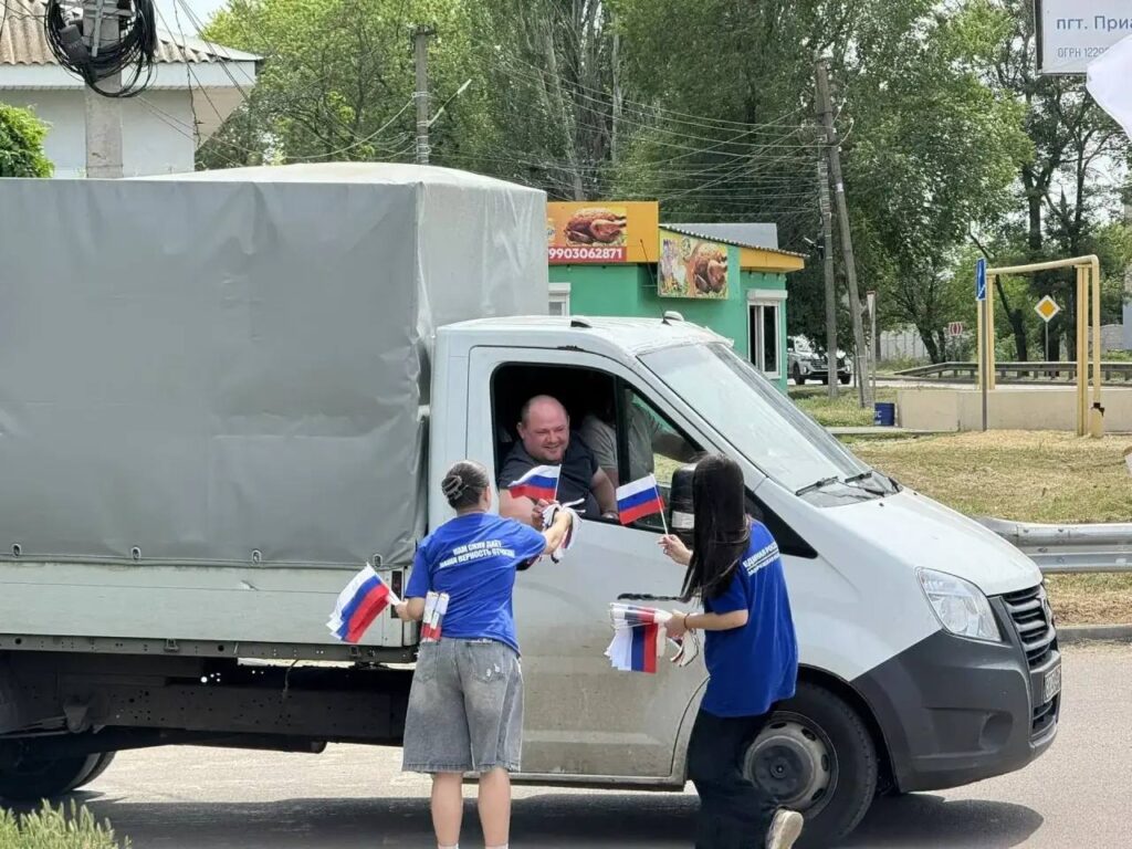Участники «Молодой гвардии Единой России» раздают российские флажки на центральной улице посёлка Приазовское Мелитопольского района Запорожской области в рамках пропагандистской акции ко Дню России
