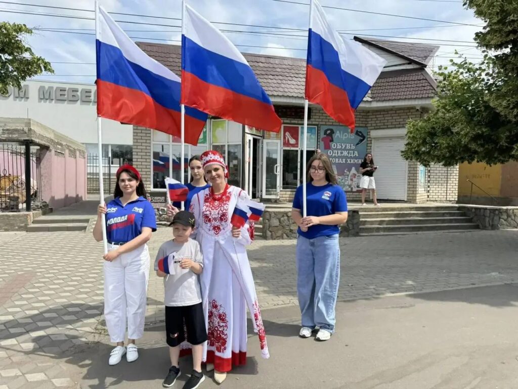 Участники «Молодой гвардии Единой России» раздают российские флажки на центральной улице посёлка Приазовское Мелитопольского района Запорожской области в рамках пропагандистской акции ко Дню России