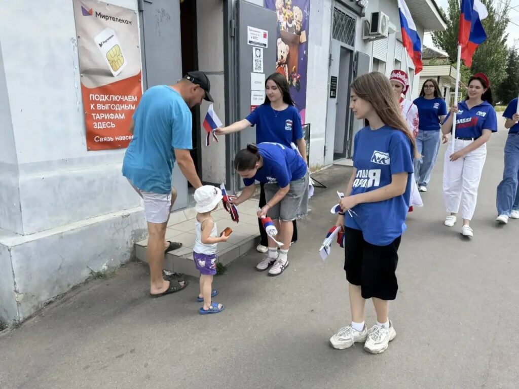 Участники «Молодой гвардии Единой России» раздают российские флажки на центральной улице посёлка Приазовское Мелитопольского района Запорожской области в рамках пропагандистской акции ко Дню России